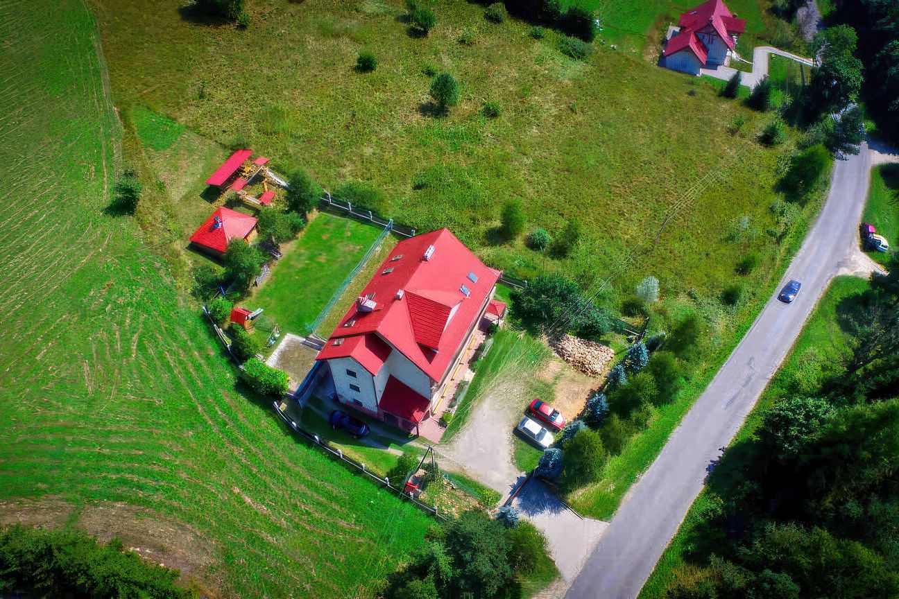 Widok z drona na Willę OdNova w Tyliczu - czerwony dach, zielone pola, las wokół